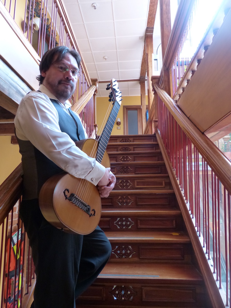 Andrés Zapico de pie con su guitarra de ocho cuerdas en una escalera de madera